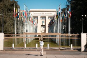 Man photographs the United Nations Office with international flags in Geneva, Switzerland.